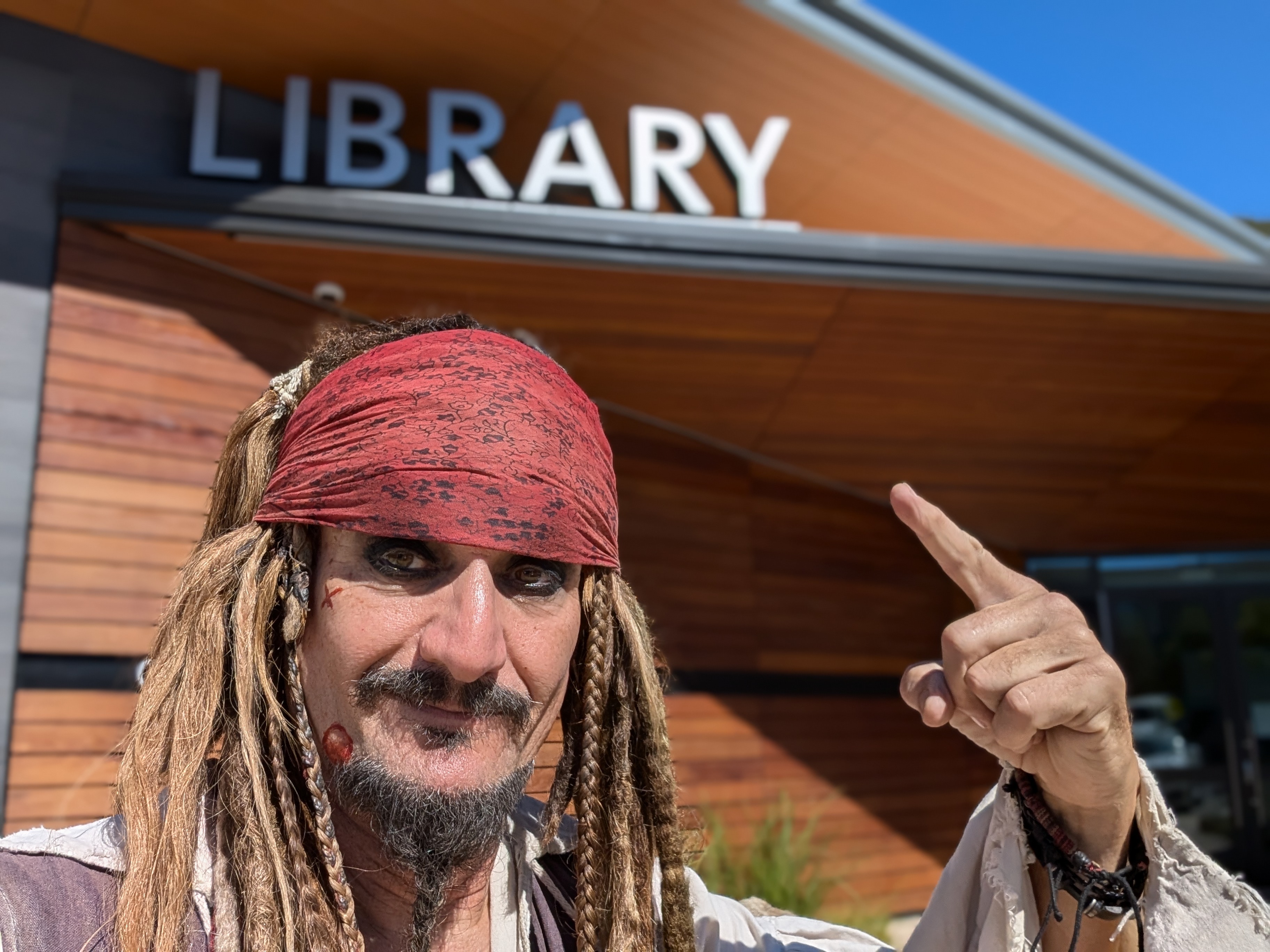 Capt'n Jack Spareribs outside a public library, pointing up at the LIBRARY sign.