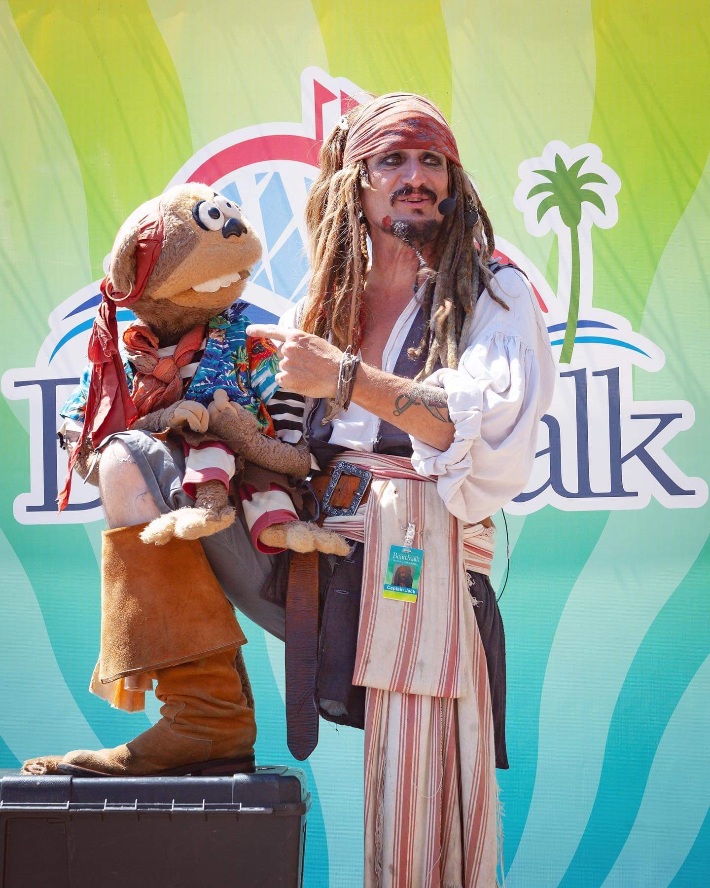 Capt'n Jack Spareribs and Maynard the Talking Monkey in front of the Santa Cruz Beach Boardwalk backdrop, wearing an official Boardwalk Entertainment credential.
