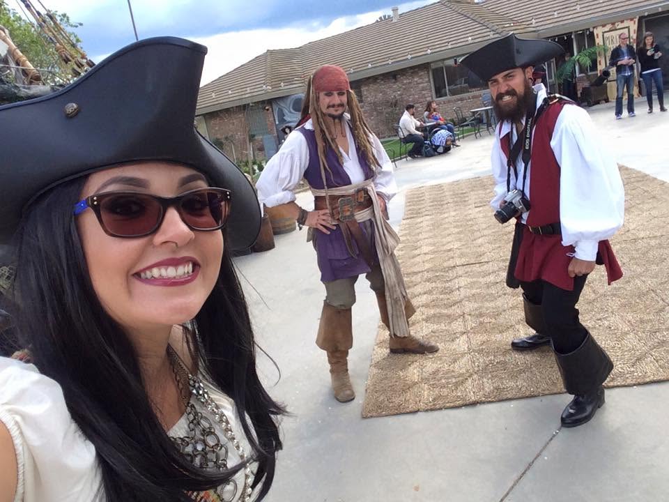 Capt'n Jack Spareribs and a fellow pirate crew member at a real backyard party, a guest taking a selfie with them in the foreground.